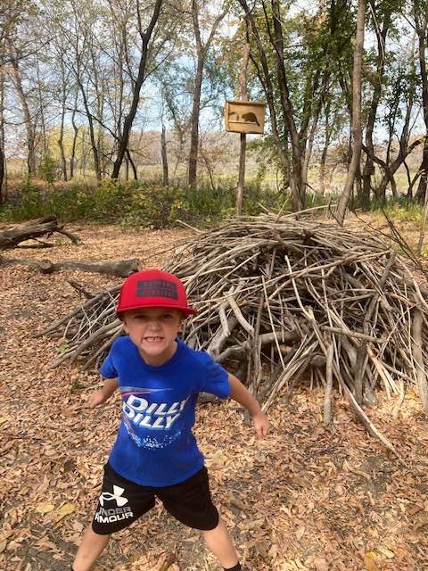 boy in front of beaver lodge built of sticks
