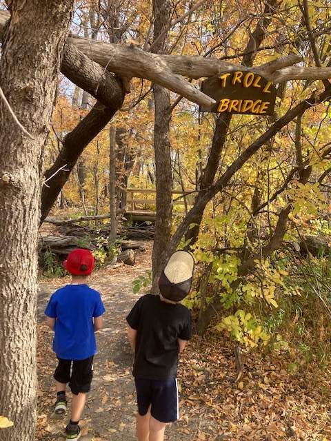  two boys on a family microadventure on a trail with a sign that says troll bridge