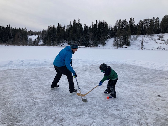 Dad and son play hockey on pond rink